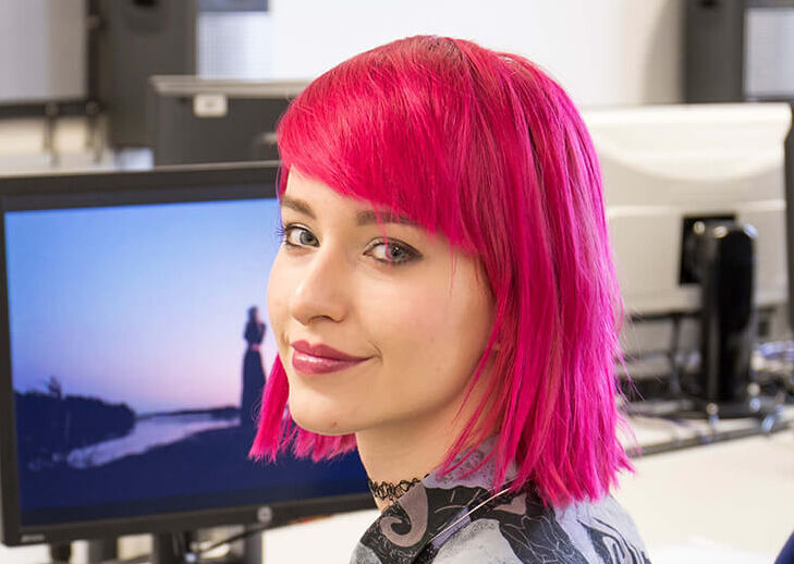 Studentin Frau sitzt vor Monitor und lächelt in die Kamer