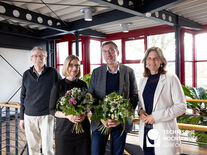 Vier lächelende Personen stehen nebeneinander und zwei von Ihnen halten Blumenstrauß in den Händen