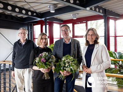 Vier lächelende Personen stehen nebeneinander und zwei von Ihnen halten Blumenstrauß in den Händen