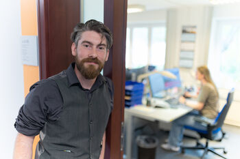 Mann mit Bart und grauem Hemd steht im Türrahmen eines Büros.