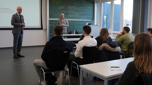 Professor steht vor der Tafel und spricht zu einer Gruppe von Studierenden