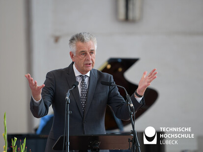 Pastor animiert zum Applaus Ein Mann steht mit ausbreiteten Armen hinter einem Rednerpult und spricht in ein Mikro