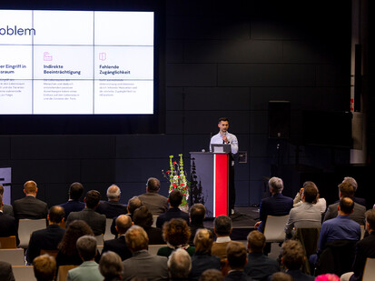 Mann steht am Rednerpult und redet zum Publikum