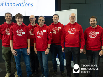 Gruppenfoto der Supportgruppe 7 Personen stehen im roten TH Lübeck Hoodie nebeneinander und lächeln