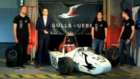 Bild zeigt vier Studenten die neben einem weißen Formula Student Wagen stehen