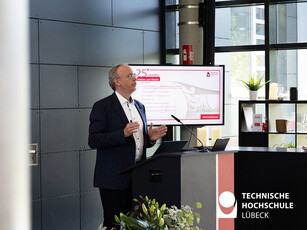Mann im Anzug und Präsentation hinter sich spricht zum Publikum