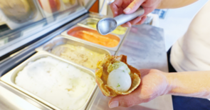 Eine Person hält eine Waffel in der Hand und lässt eine Kugel Eis hineinfallen