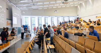 Hörsaal mit vielen Menschen, eine lange Schlage bildet sich vorm Rednerpult