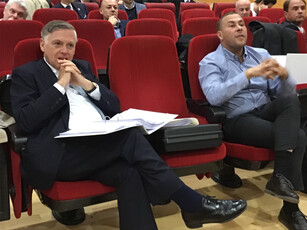 Two men listen intently while sitting in the audience of a lecture hall.