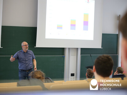 Vorstellung der Lübecker Stadtwerke Mann steht im Hörsaal und spricht zum Publikum und im Hintergrund eine Präsentation