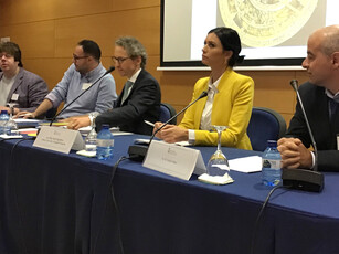 Five people at a panel discussion; a woman in a yellow blazer is speaking.