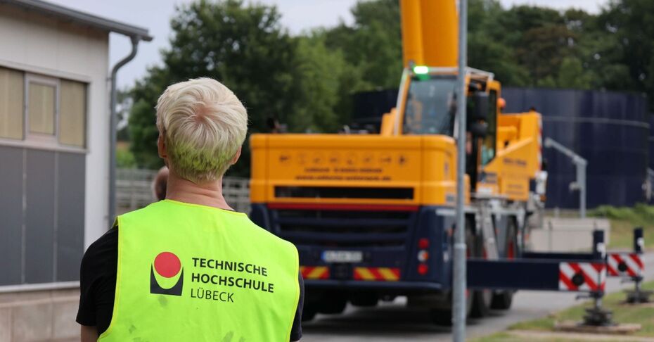 Hinteransicht eines Mannes mit TH-Lübeck-Warnweste vor einem Kran