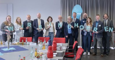 Elf Personen präsentieren im Konferenzraum den 3D-Schriftzug WIR SIND HOEREN.