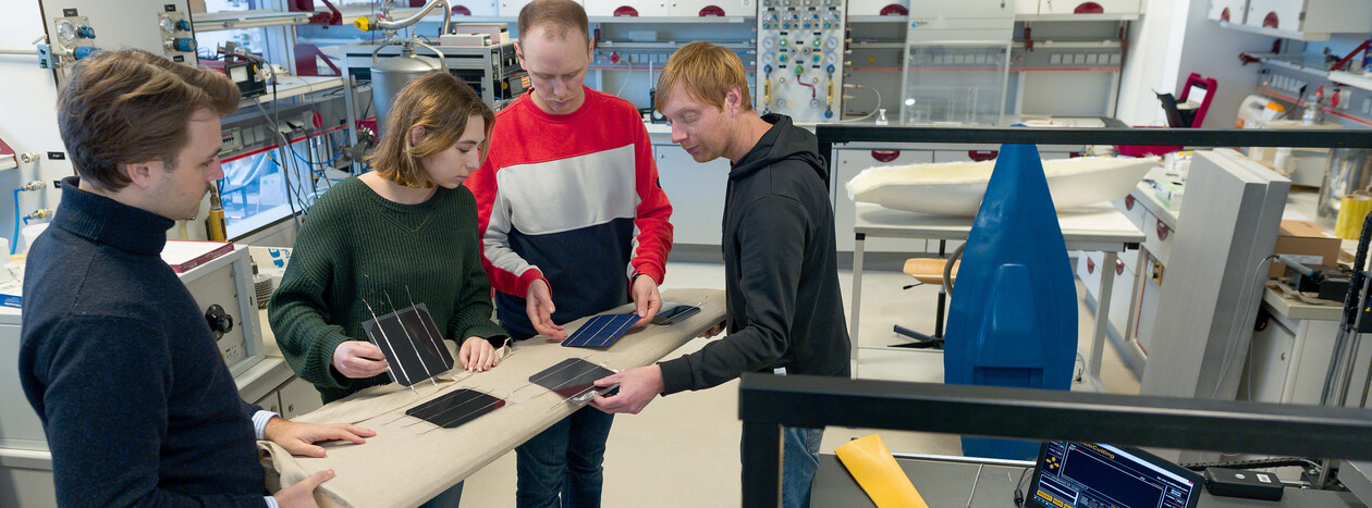 Four researchers, including one woman, stand around a table in a laboratory, collectively examining several small solar panels for a project.