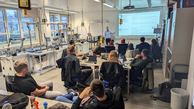 Studierende und Dozent im Laborraum der TH Lübeck während eines praxisorientierten Vortrags über 3D-Druck und Automatisierungstechnik.