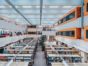 Auf diesem Bild blickt man von oben auf Bücherregale hinunter und sieht orangefarbene Gruppenarbeitsräume
