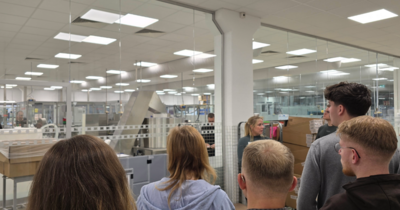 Personen blicken durch eine Glaswand in eine saubere Produktionshalle.
