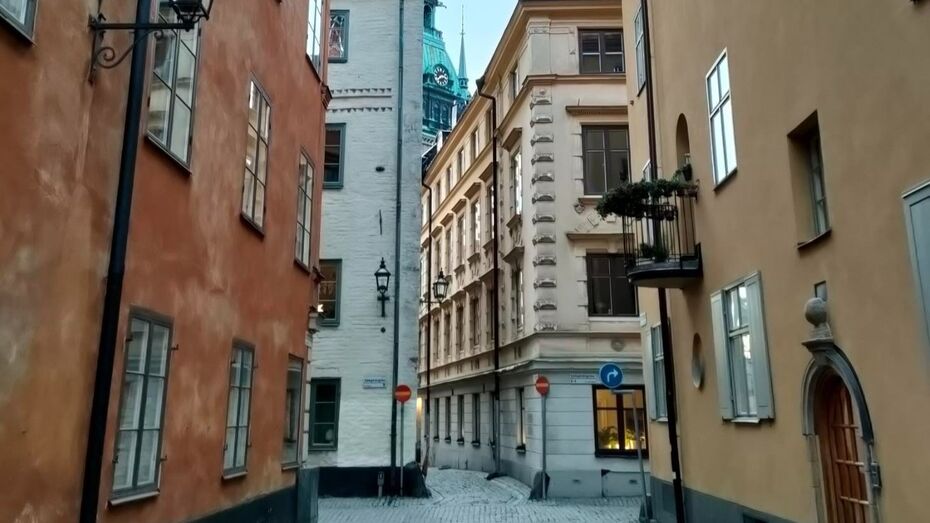 Alte Gebäude stehen auf beiden Seiten einer engen Gasse. Es ist nur wenig Himmel zu erkennen, der auch noch von einem Kirchturm mit grünem Dach verdeckt wird.