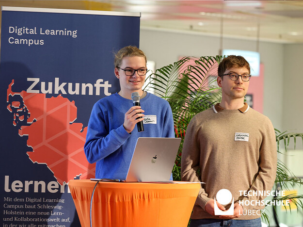 Vortrag über den Digital Learning Campus Zwei Männer stehen am Rednerpult und einer hält ein Mikrofon