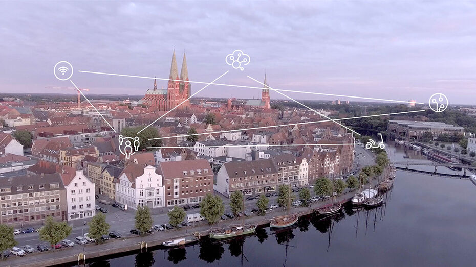 ['English'] Eine Luftaufnahme der Lübecker Altstadtinsel. Smart-City-Icons schweben über den Dächern der Stadt und sind über ein Netz an Linien miteinander verbunden.
