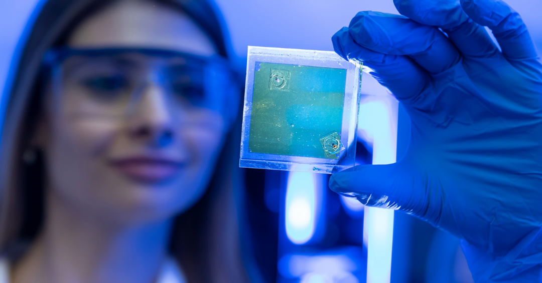Forscherin mit Schutzbrille hält eine transparente Dünnschicht-Solarzelle.