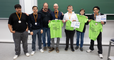 Siegerteam mit Medaillen zeigt stolz grüne Wettbewerbs-Shirts und Urkunden.