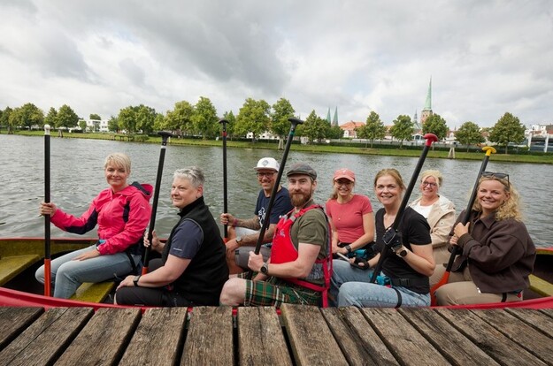 Fröhliche Gruppe sitzt im Kanu auf einem Fluss und hält die Paddel hoch.