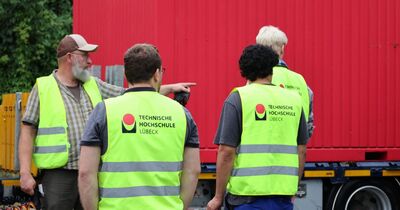 Vier Männer mit gelben Warnwesten der TH Lübeck stehen vor einem roten Container