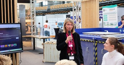 Eine Frau steht mit einem Mikrofon an einem Messestand.