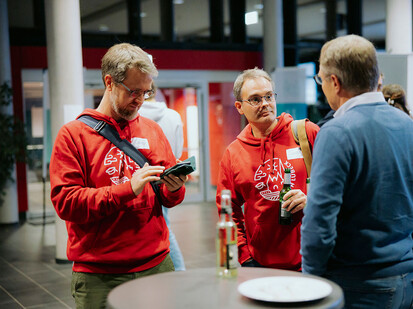 Austausch bei der Ausstellung Zwei Personen sprechen miteinander während eine dritte auf ein Handy guckt