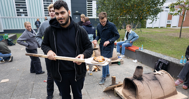 Student präsentiert Pizza Student in schwarzer Jacke präsentiert Pizza auf Pizzaschieber