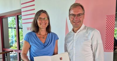 Frau Helbig und Herr Wendt halten lächelnd die Urkunde in den Händen