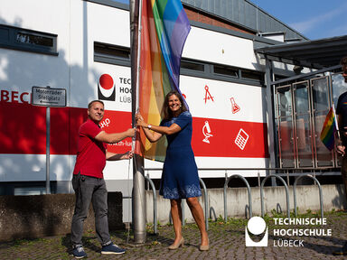 Christian Till und Muriel Helbig hissen gemeinsam die Regenbogenflagge vor Gebäude 2 der TH Lübeck. Sie gesellt sich neben die Friedensflagge. Foto: TH Lübeck 