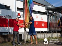 Christian Till und Muriel Helbig hissen gemeinsam die Regenbogenflagge vor Gebäude 2 der TH Lübeck. Sie gesellt sich neben die Friedensflagge. Foto: TH Lübeck 