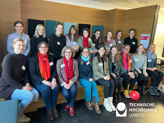 Gruppenfoto der Mentorinnen 18 Frauen sitzen auf einer großen Sitzbank mit zwei Ebenen und lächeln in die Kamera