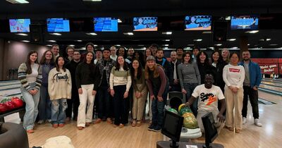 Internationale Studierende stehen in einer Gruppe vor einigen Bowlingbahnen zusammen und lächeln in die Kamera.