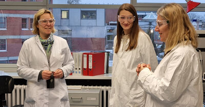 Drei Frauen in weißem Kittel mit Sicherheitsbrillen in einem Labor