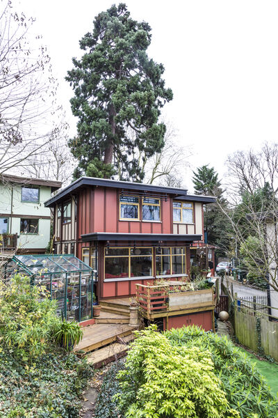 Zweistöckiges Holzhaus mit roter Fassade und angebautem Gewächshaus.