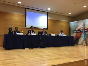 Four men sitting at a long table during a panel discussion on a stage.
