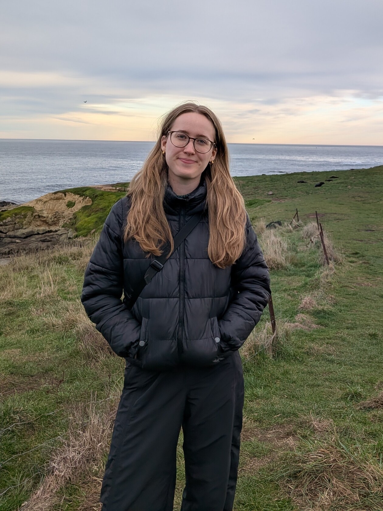 Studentin steht auf einer Küstenwiese in Neuseeland mit Meerblick im Hintergrund