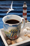 Tasse Kaffee auf Sand mit Steinen und Leuchturm