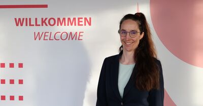Wibke Düsterhöft-Wriggers Eine Frau steht vor einem hellen Hintergrund mit der Schrift "Willkommen".