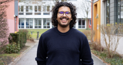Ein Mann mit braunen Locken und Brille lächelt in die Kamera