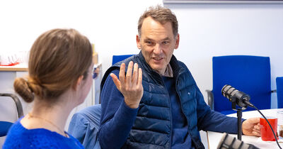 Eine Frau im Vordergrund und ein Mann, der gestikuliert im Hintergrund 