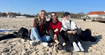 Drei Studierende sitzen im Sand am Strand der Ostsee. 