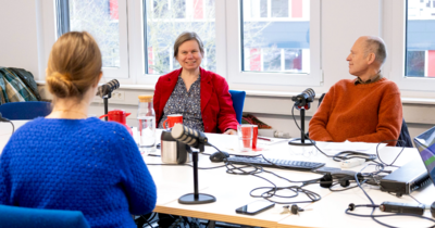 Drei Personen sitzen an einem Tisch und unterhalten sich bei einem Podcast miteinander