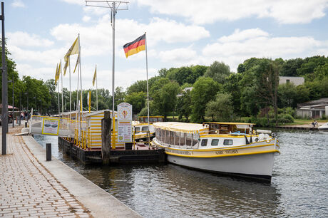 Weiß-gelbes Ausflugsschiff liegt am Anleger neben einem Kassenhäuschen.