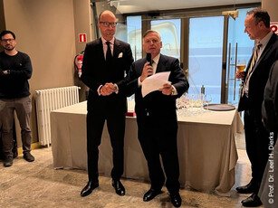 A man gives a speech with a microphone at a reception while another man listens.
