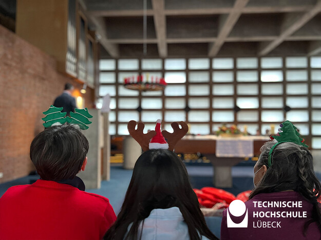 Drei Personen werden ab den Schultern von hinten gezeigt und sie tragen weihnachtlichen Kopfschmuck