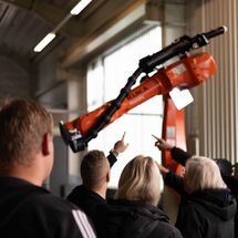 5 Personen stehen vor Industrieroboterarm und zwei zeigen drauf